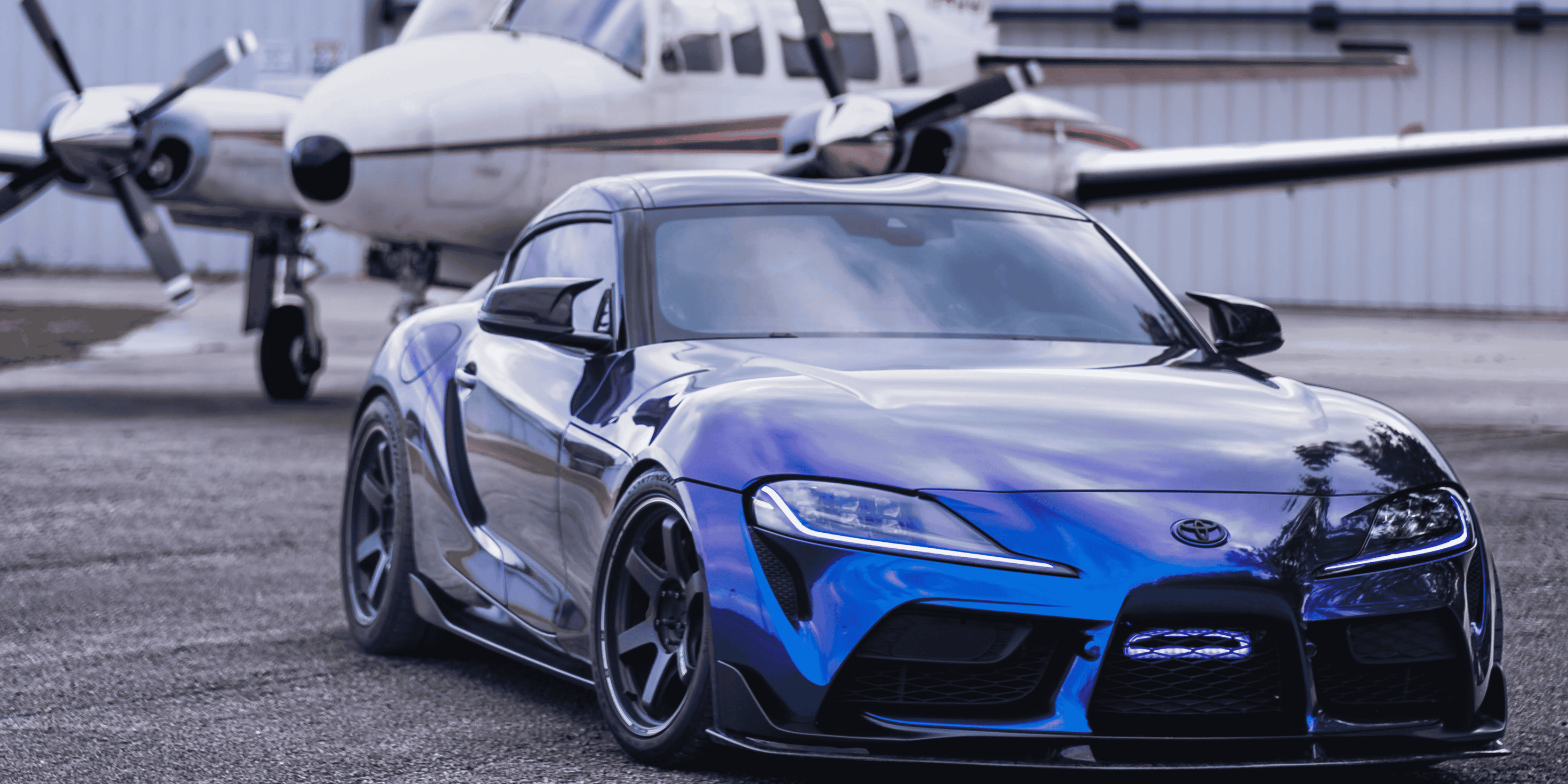 Blue sports car on a runway with a small airplane in the background